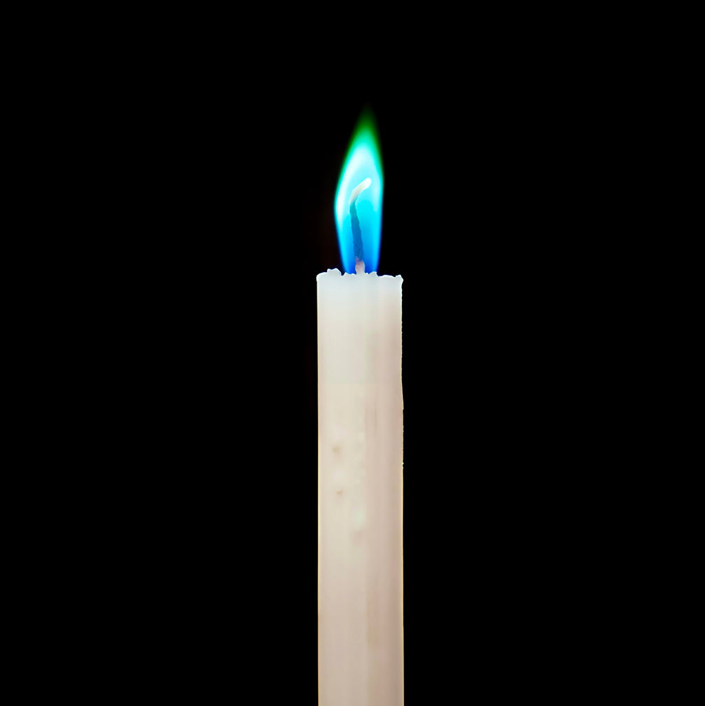 Biala swieca z kolorowym niebiesko-zielonym plomieniem na czarnym tle
