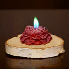 Bordowa roza swieca z niebiesko-zielonym plomieniem na bialym drewnianym plastrze