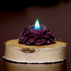 Ciemnofioletowa swieca w ksztalcie rozy z niebiesko-zielonym plomieniem na drewnianym krazku