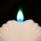 Biala swieca w ksztalcie muszli z niebiesko-zielonym plomieniem na czarnym tle