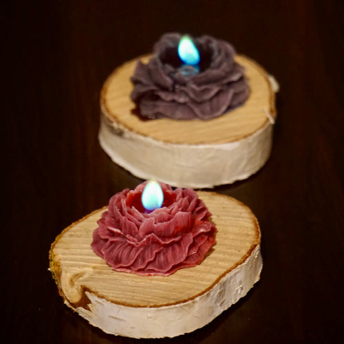 Dwie rozane swiece: bordowa i ciemnofioletowa z niebiesko-zielonym plomieniem na drewnianych krazkach