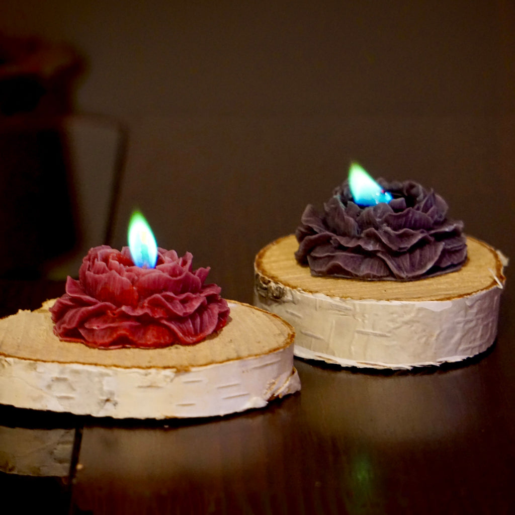 Dwie rozane swiece: rozowa i ciemnofioletowa z zielono-niebieskim plomieniem na bialych krazkach drewna